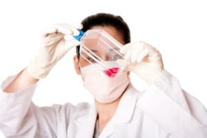 Female scientist researcher looking at red tissue cell culture medium in flask wearing gloves and mouth cap, isolated.
