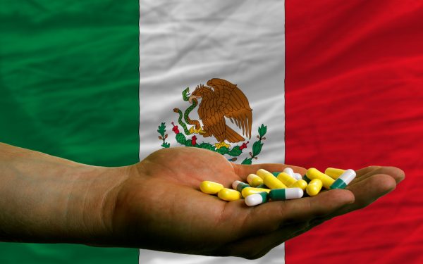 man holding capsules in front of complete wavy national flag of mexico symbolizing health, medicine, cure, vitamines and healthy life